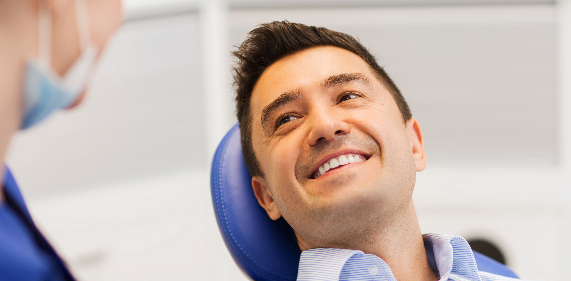 A person is seated in a dental chair, receiving care from a dental professional who stands behind them.